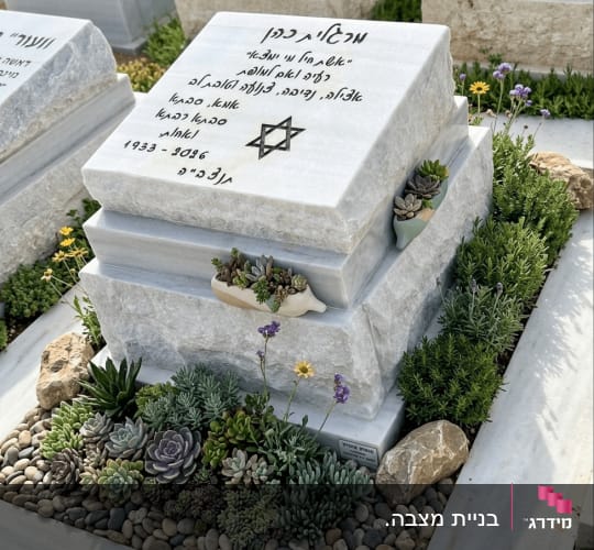 מצבה עם כיתוב בעברית וצמחים מסביב